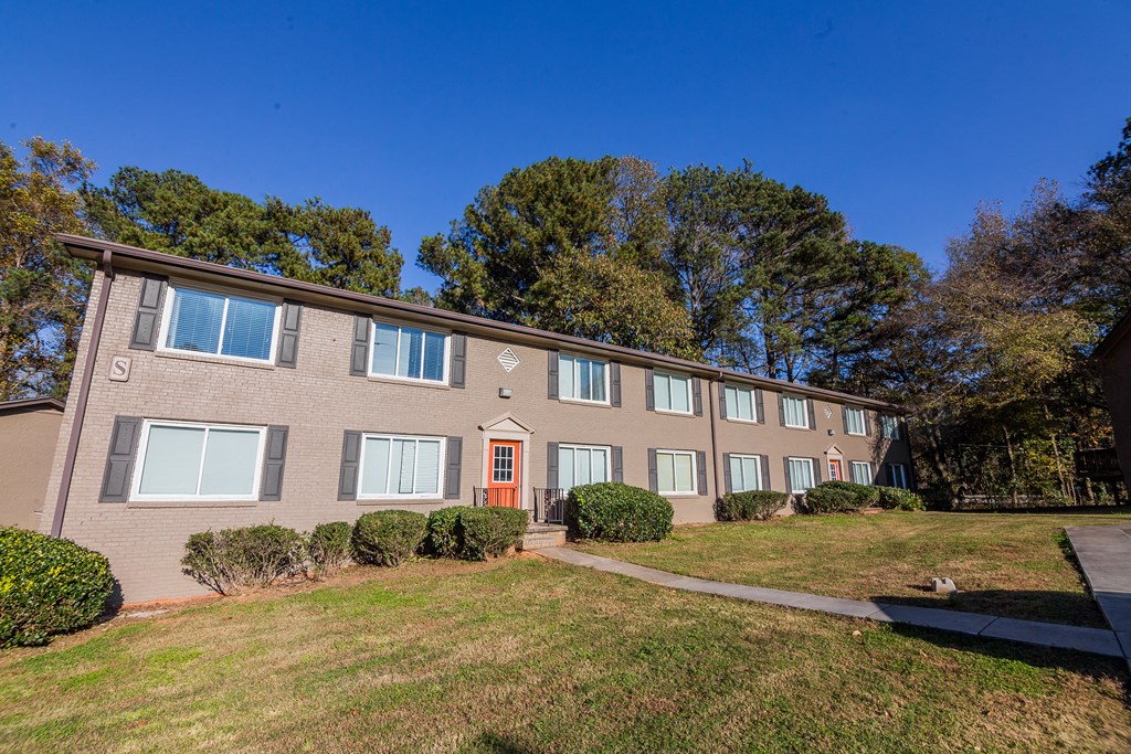 a brick apartment building with a green lawn and trees in the background at Broadway at East Atlanta, Atlanta